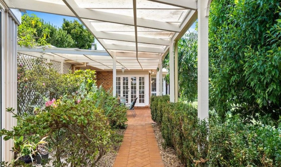 Covered garden walkway painted white, leading along a brick path to a home's painted French doors