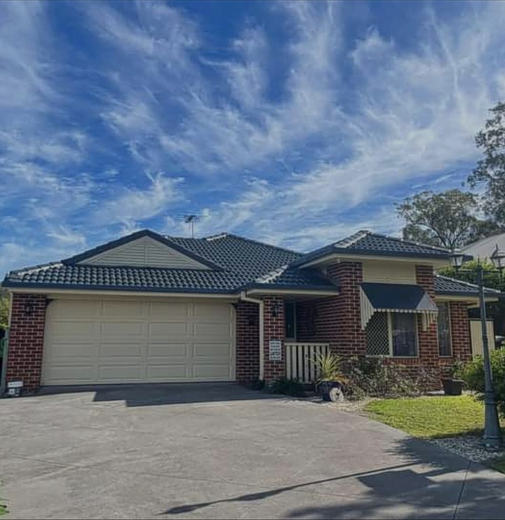 Brick Toowoomba home with a cream repainted garage door and dark charcoal tiled roof under a wide streaked sky