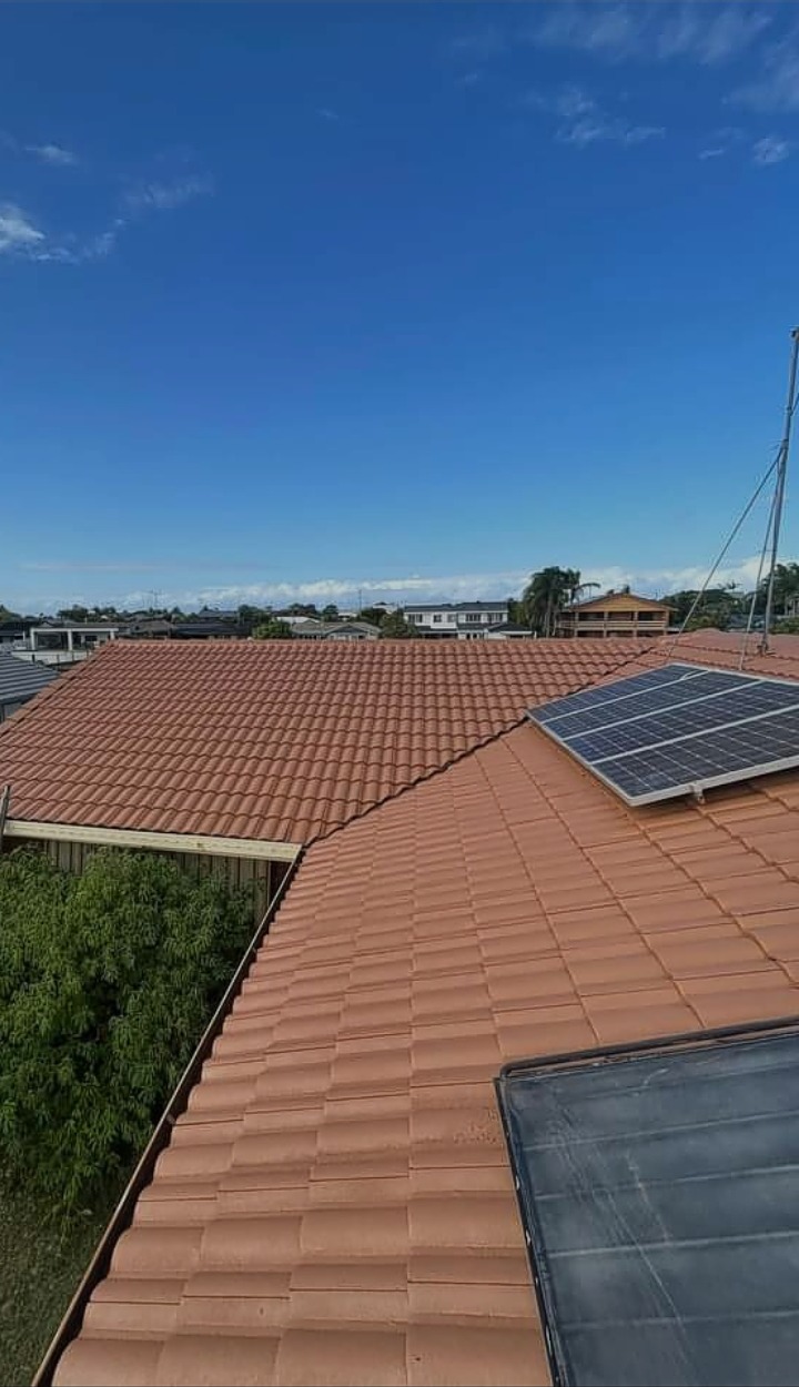 Elevated view across a large terracotta tiled roof in Toowoomba freshly coated, solar panels on the far pitch and suburb rooftops behind