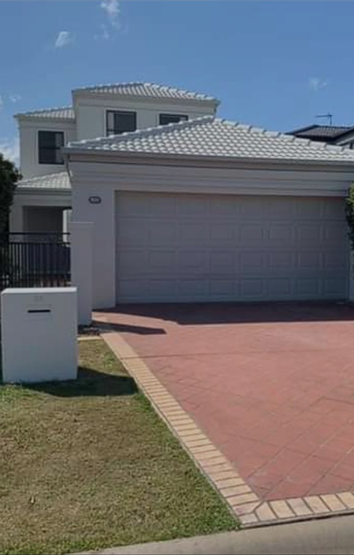 Two storey rendered Toowoomba home with a freshly painted white garage door and pale tiled roof, brick paved driveway in front