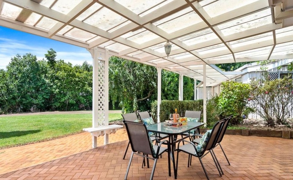White painted pergola over a brick paved patio with an outdoor dining setting, looking out to the garden