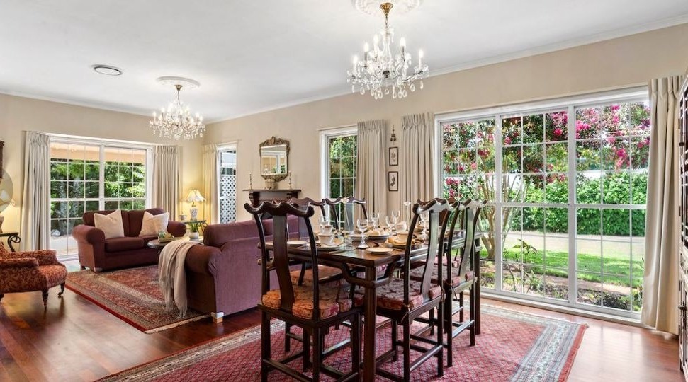 Formal dining and living room with cream painted walls, white trimmed sash windows and glazed doors opening onto a garden